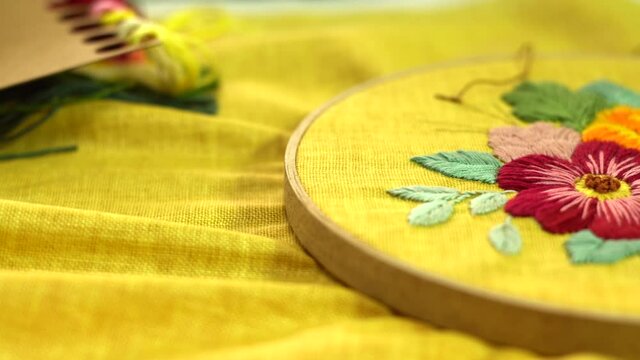 Beautiful embroidery flowers on cotton fabric. Product of needlework on a piece of embroidery. Needlework is decorative sewing and textile arts handicrafts. How to stitch embroider flowers on clothes.