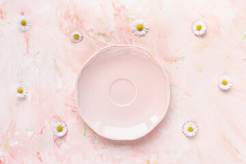 Empty ssmall plate on pastel pink and fresh summer daisy flowers, minimalistic background. tea party, drinking coffee or dessert recipe concept. Top view, flat lay, copy space