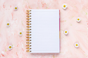 Open notepad and fresh spring daisy flowers, pastel background, woman desk workspace. Spring lifestyle concept. To Do List template, empty page, mock up. Minimalist flat lay, top view, copy space