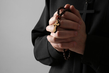 Priest with rosary beads praying on grey background, closeup. Space for text