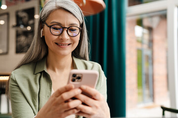 Mature smiling woman using earphone and mobile phone in cafe