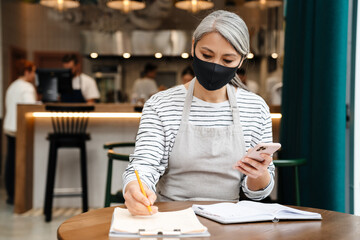 Mature waitress woman using cellphone while working at table