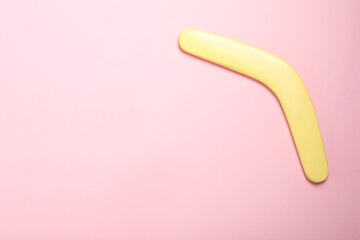 Yellow wooden boomerang on pink background, top view. Space for text