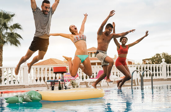 Multiracial friends having fun jumping inside swimming pool during summer vacation - Travel and party concept - Main focus on center girl body - Powered by Adobe
