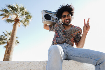 African american man listening music with vintage boombox stereo outdoor on the beach - Summer...