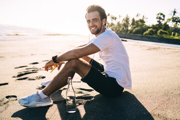 Cheerful man listening to music in earphones on sandy beach
