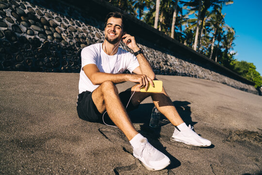 Cheerful man with smartphone enjoying music from earphones on beach
