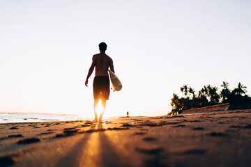 Rear view of sportive man walking at summer seashore with sunset spending day for practice hobby...