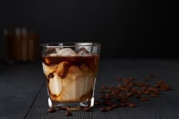 Bracing Iced coffee in a glass on a wooden painted table with coffee beans and dark background. Cool summer drink concept.
