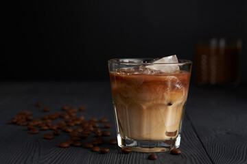 Bracing Iced coffee in a glass on a wooden painted table with coffee beans and dark background. Cool summer drink concept.