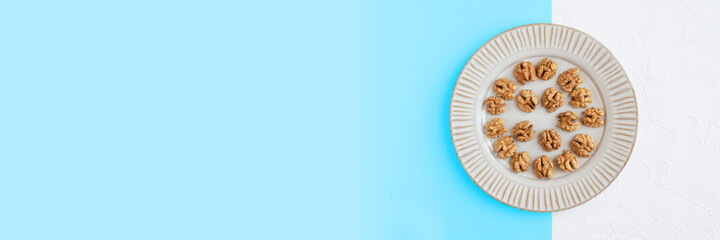 Walnuts in a plate on blue and white background, top view, banner.