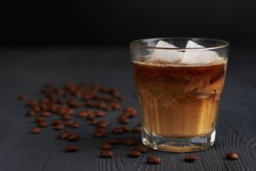 Bracing Iced coffee in a glass on a wooden painted table with coffee beans and dark background. Cool summer drink concept.