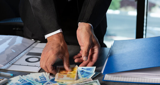 Businessman's Hands holding a fan of money of Israeli New Shekels. Stack of Money scattered (Currency of usa dollar, nis banknotes) on the table. Cropped image of Hand holds banknotes. Selective focus