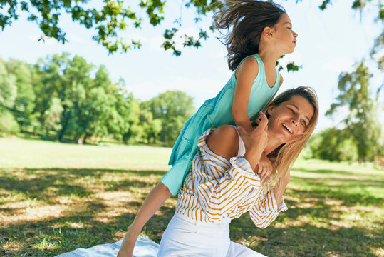 Horizontal image of happy loving mother and her cute daughter playing in the park during the picnic. Playful pretty woman and little girl spending time together on a sunny day. Mom and kid have fun.