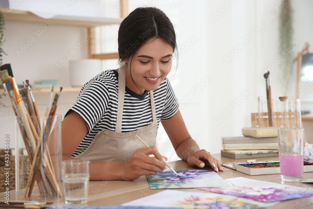 Wall mural young woman drawing flowers with watercolors at table indoors