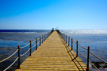 Naklejka premium The skyline is where the wooden bridge leads to the pier. Red flag as a sign that the entrance is closed, it is dangerous to be in the sea. Sunset at the sea. Vacation concept