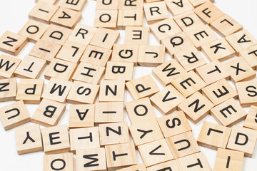 Letras del alfabeto en piezas de scrabble de madera esparcidas sobre un fondo blanco. Vista superior