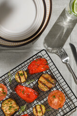 Vegetables grilled (zucchini, eggplant,tomato and sweet pepper) are on grill. Plates, fork, knife and glass stand next to them.