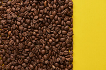 Roasted coffee beans on yellow background with copy space. Close up top view.