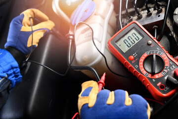 Car mechanic in service center using multimeter detail.