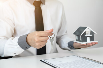 Home insurance agent holding a house model and a key in the office.