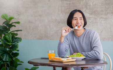 Portrait of happy handsome asian man eating breakfast in a cafe hotel. Young nerdy man with healthy clean food salad and juice on the dining table. Modern healthy food lifestyle holiday concept