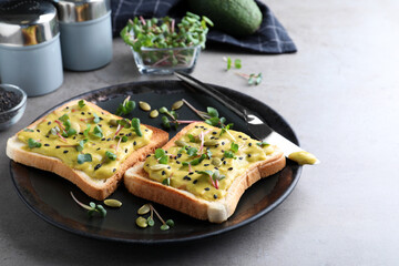 Delicious sandwiches with guacamole, seeds and microgreens on grey table