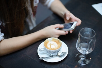 Girl entering pin code on phone while sitting in cafe with fresh cappuccino