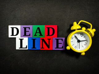 Text DEADLINE with colorful wooden jigsaw and alarm clock on black background.