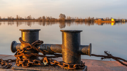 Mooring bollard on the mole with sunset river on the background. Space for text.