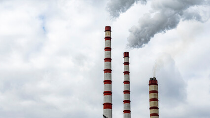 Industrial smoke from chimney on dramatic sky background. View of high chimney pipes with grey...
