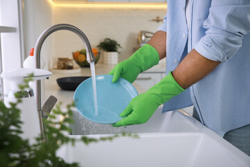 Man washing plate above sink in kitchen, closeup