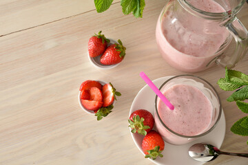 Glass and jug of strawberry milkshake on wooden table elevated