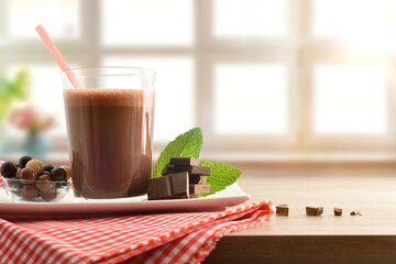Glass with chocolate milkshake on plate with tablecloth front isolated