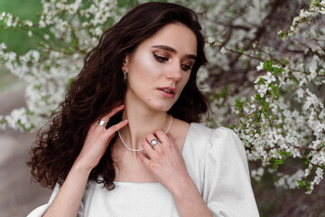 Spring lifestyle. Model posing near white blooming trees without mask outdoor countryside. Dreaming girl with curly hair.