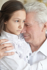 Portrait of sad grandfather and granddaughter hugging at home