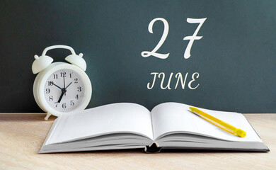 june 27. 27-th day of the month, calendar date.A white alarm clock, an open notebook with blank pages, and a yellow pencil lie on the table.Summer month, day of the year concept