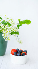 Summer berries: strawberries, blueberries on the background of a bouquet of blooming bird cherry. Image with selective focus
