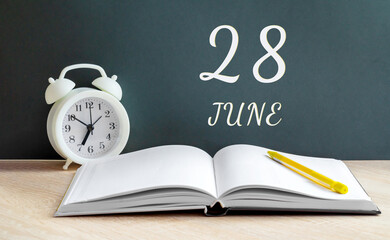 june 28. 28-th day of the month, calendar date.A white alarm clock, an open notebook with blank pages, and a yellow pencil lie on the table.Summer month, day of the year concept