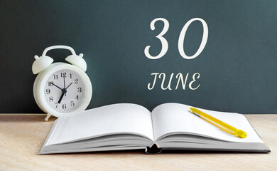 june 30. 30-th day of the month, calendar date.A white alarm clock, an open notebook with blank pages, and a yellow pencil lie on the table.Spring month, day of the year concept