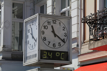 square clock in a public space indicating time and temperature. Translation of the text = new...