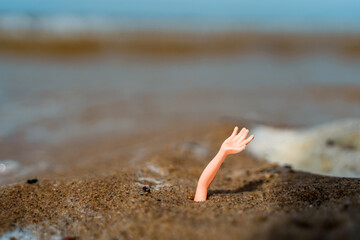 Concept photo of a toy hand sticking out of the sand on the beach