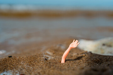 Fototapeta na wymiar Concept photo of a toy hand sticking out of the sand on the beach