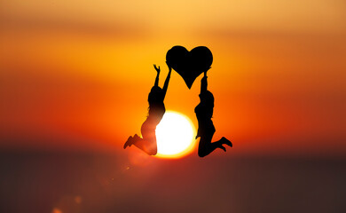 Zwei Frauen hüpfen mit einem Herz vor sonnenscheibe