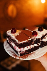 Close-up of a piece of chocolate cake with milk cream. The treat lies on disposable tableware. Takeaway food. Dessert in a cafe or restaurant.