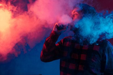 Adult person vaping in studio with colored lights. man using electronic cigarette and exhaling...