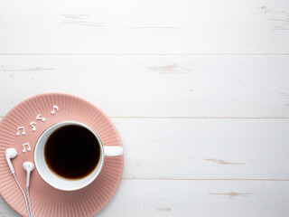 イヤフォンと音符とコーヒーが乗ったピンクの皿白木背景