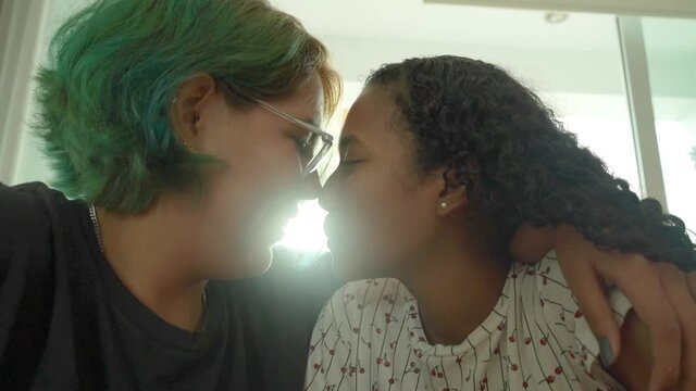 Pareja joven de lesbianas se miran cara a cara para darse un beso en contraluz