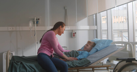 Mother visiting son lying in bed in hospital ward