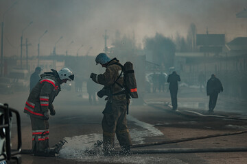 a team of rescuers extinguish a fire in the house. firefighters pour water on the raging flames. smoke and smog from the burning building